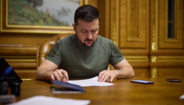 Man seated at a wooden desk signing papers with a focused expression in an ornate room, tablet and phone nearby.