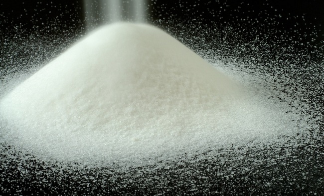 A Mountain of Granulated Sugar on a Black Background - Pure, snowy white mountain of sugar on a black textured background with a soft mist of sugar granules falling on the top.